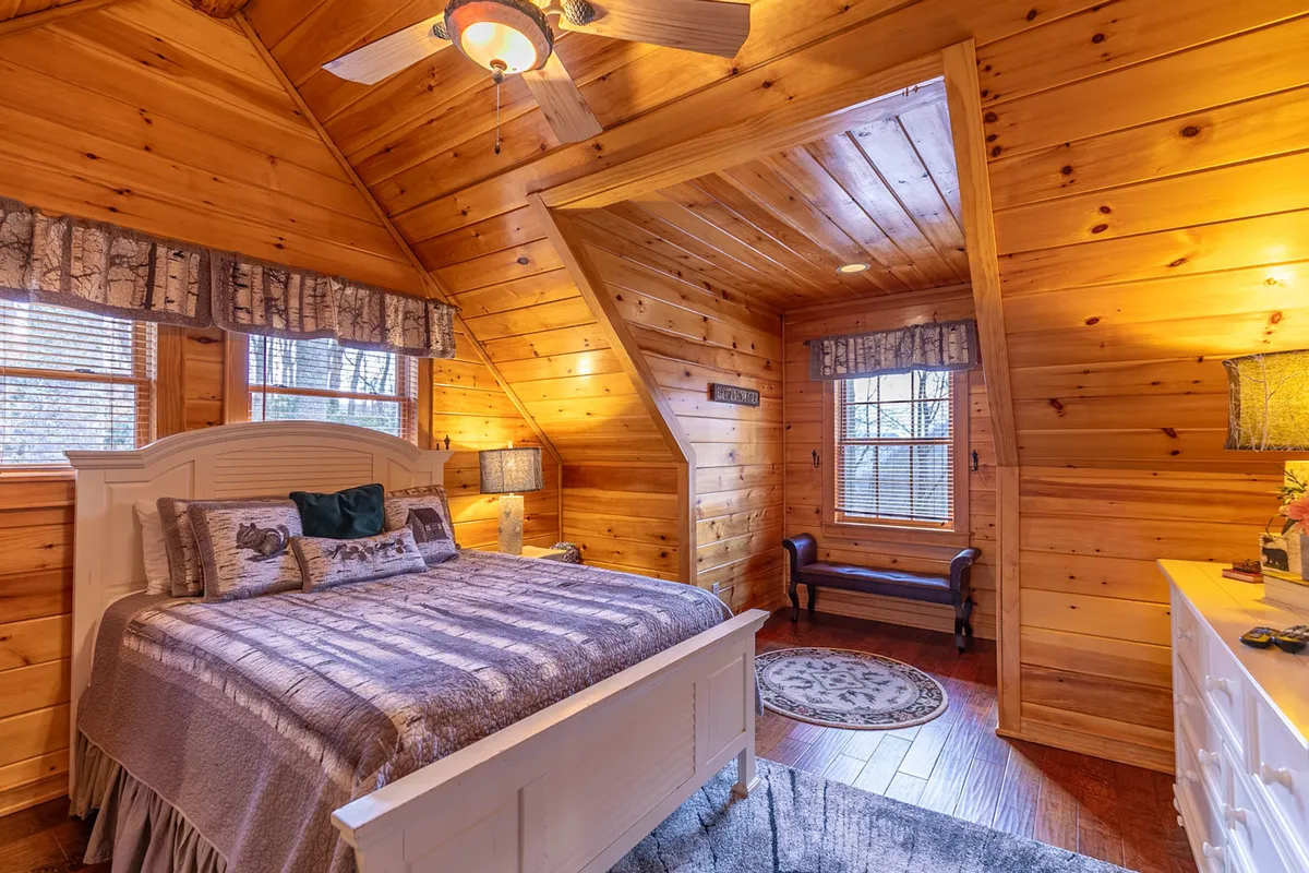 This bedroom features a cozy bed with decorative pillows, a wooden ceiling, and a window that draws in natural light. A side table with a lamp adds to the warm, welcoming feel, inviting guests to relax or enjoy quiet moments.