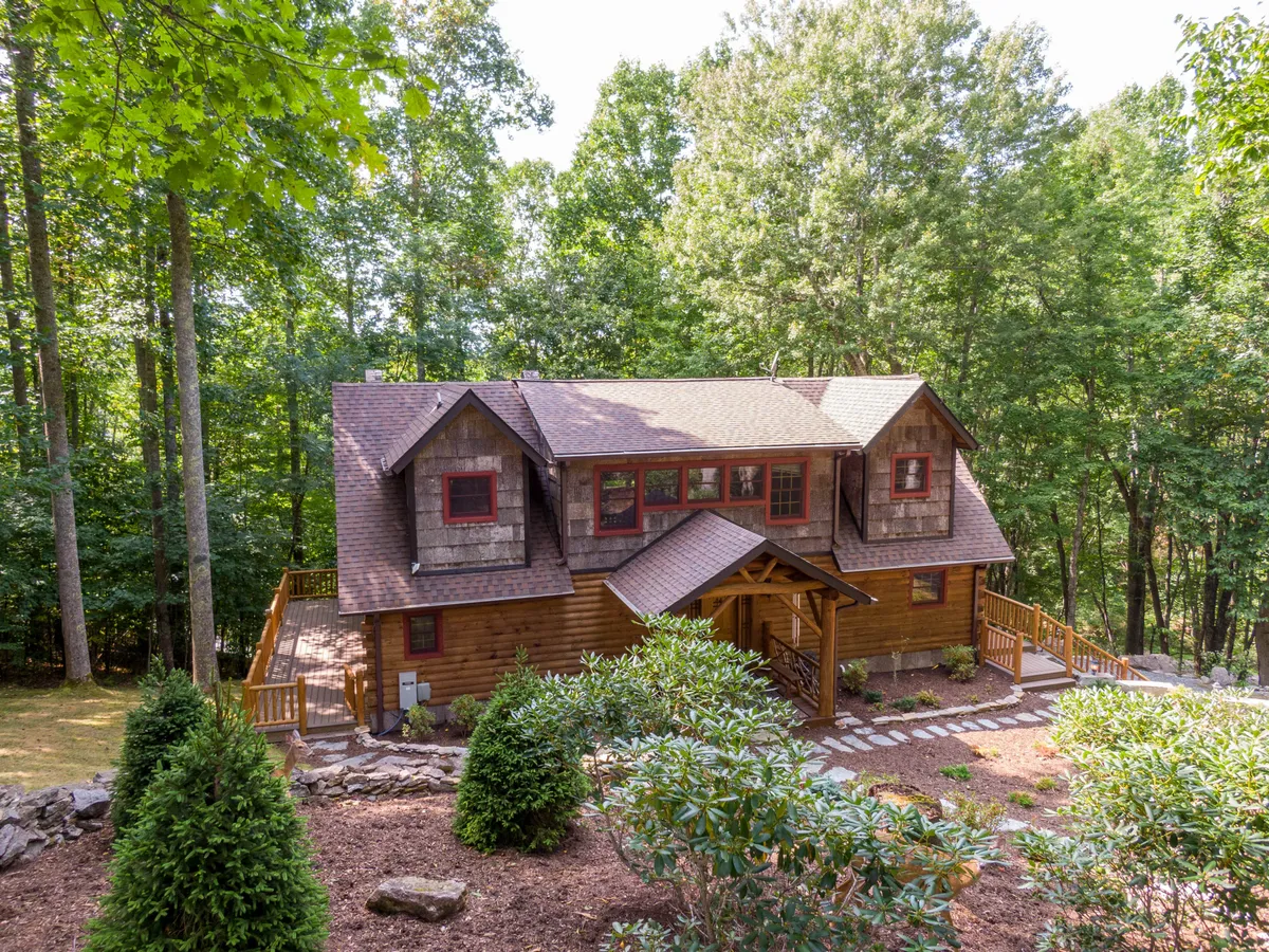 A broad exterior view of the lodge shows its wooden façade, stone pathway, lush surrounding greenery, and large windows with red accents. The porch entryway invites guests into a welcoming space ideal for family get-togethers and outdoor activities.