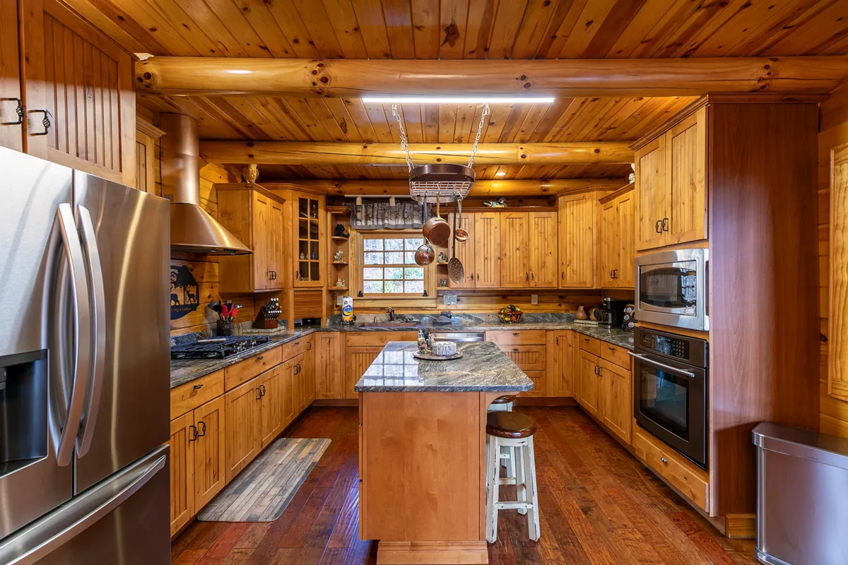 This image showcases a spacious kitchen with a stunning granite countertop island, rich wood cabinetry, and premium stainless steel appliances. The island includes comfortable bar seating, creating a perfect gathering spot for meal prep or casual breakfasts. Warm lighting and cozy decor enhance the inviting atmosphere.