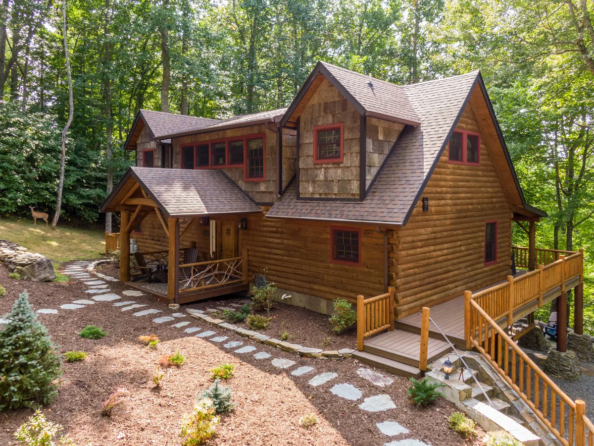 The hero image showcases a classic log cabin nestled in lush greenery, with a spacious wooden deck and a stone pathway leading up to the inviting porch. The scene exudes warmth and tranquility, highlighting the cabin's rustic charm and its seamless integration with the surrounding natural beauty. The outdoor space is perfect for relaxing, spotting wildlife, or gathering with loved ones under the stars.