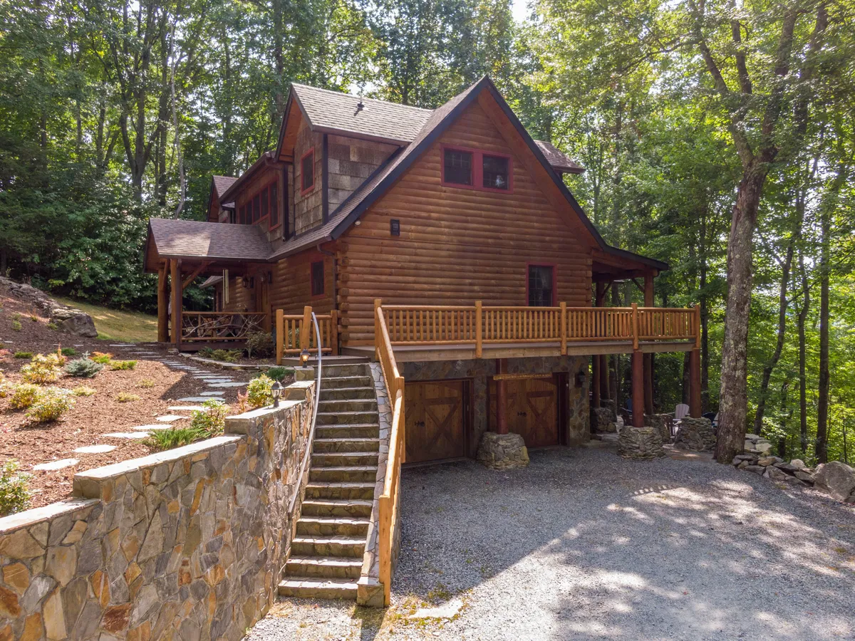 This image captures the log cabin structure of Running Waters Lodge, featuring a spacious wooden deck and stone steps surrounded by mature trees. The deck offers ample space for outdoor gatherings, relaxation, and enjoying the natural mountain environment.