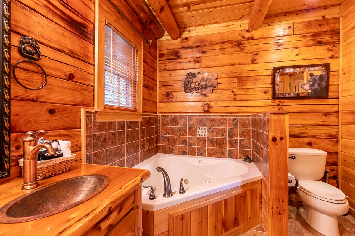 A luxurious bathroom scene featuring a Jacuzzi tub surrounded by warm wooden cabinetry and whimsical bear-themed artwork. The space feels inviting and spa-like, perfect for unwinding after a day of adventure.
