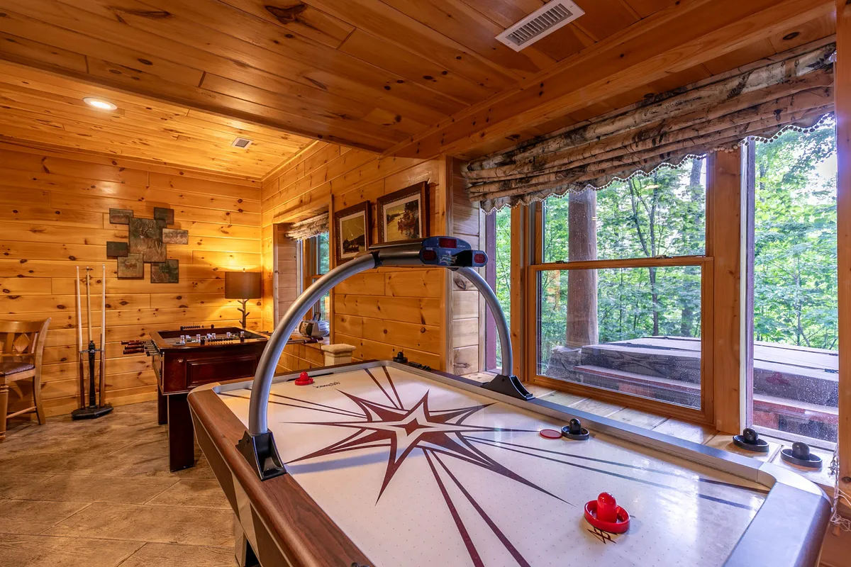 A playful basement space with an air hockey table set against wooden paneling and large windows. Artwork and a table lamp add a cozy touch, while the setup is clearly designed for interactive entertainment and group fun.