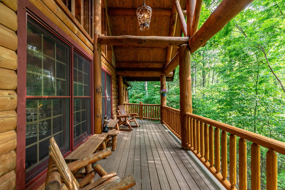 A tranquil exterior deck scene featuring wooden railings, hanging lanterns, and inviting rocking chairs surrounded by lush nature. The space looks out onto the serene mountain landscape, creating a peaceful spot to unwind, enjoy the sunrise, or stargaze at night.